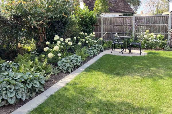 Bistro set on small round patio in corner of lawn with Raj Breen sandstone coping as mowing strip. Built by JG Landscaping***Designed by Wilson Associates Garden Design, www.wilsongardendesign.co.uk | Built by JG Landscaping, www.jglandscapinguk.com
