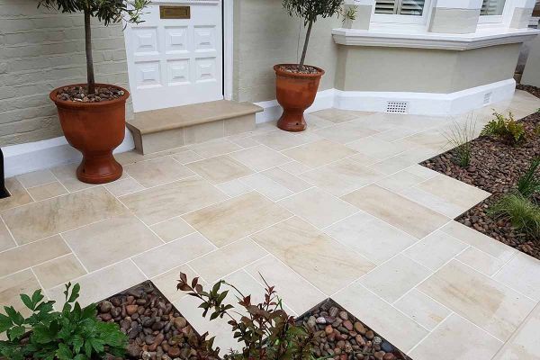 Path of Multi Mint sawn paving slabs with pale joints leads to wide paved area with step up to front door of bay-windowed house.***Crocus Landscapes, www.crocuslandscapes.co.uk