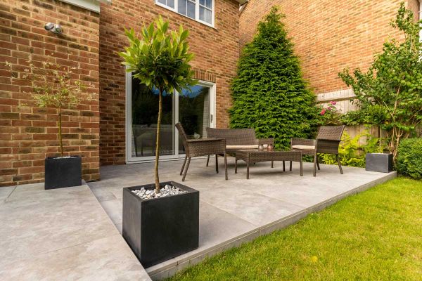 Small Silver Contro Porcelain-paved relaxation area with rattan furniture and square planters next to sliding doors into house.***Gadsden Gardens, www.facebook.com/GGLandscapers | Photography by Brian Devonshire