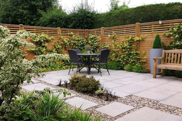 Patio of Silver Grey granite paving in corner of fenced garden, with variegated plants in borders and clipped fir in tall pot.***Rhoda Maw Garden Design, www.rhodamaw.com
