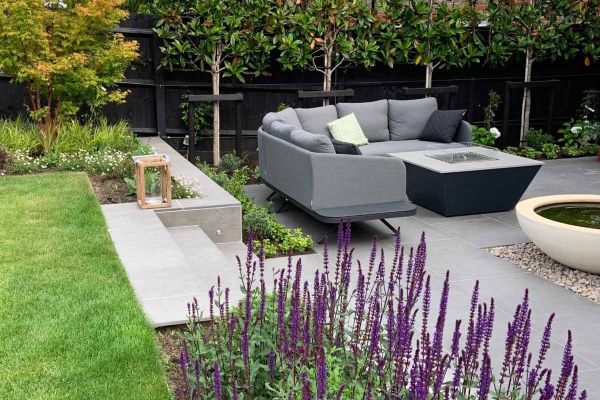 Steel Grey porcelain steps with smooth coping lead down to patio area with garden furniture, fire-pit and water feature.***Designed by Rosemary Coldstream Garden Design, www.rosemarycoldstream.com | Built by Landesigns, www.landesigns.co.uk
