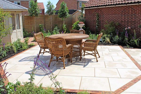Wicker dining set on Venetian Beige vitrified paving set with clay pavers between garden house, slatted fencing and garage wall.***Image also displays Cotswold Clay Pavers | Essex Garden Designs, www.essexgardendesigns.co.uk
