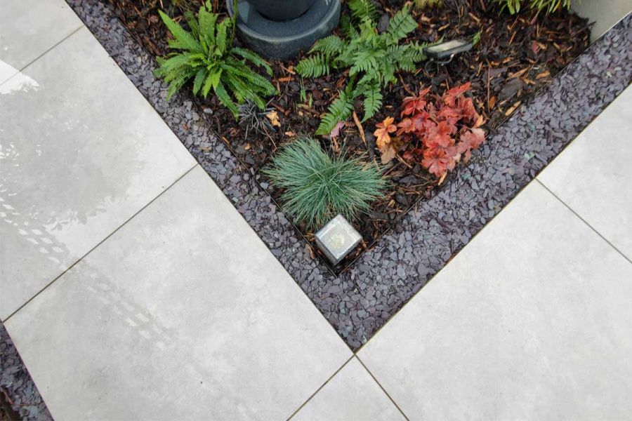 Aerial view of corner of bed with low plants and gravel edge, set in 800x800 Polvere porcelain paving. Design by Floral and Hardy.