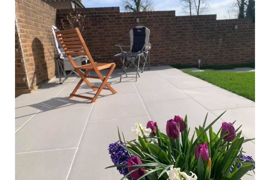 Florence Grey porcelain patio laid in corner of walled garden, seen over pot of purple tulips. Design by A and G Gardening.