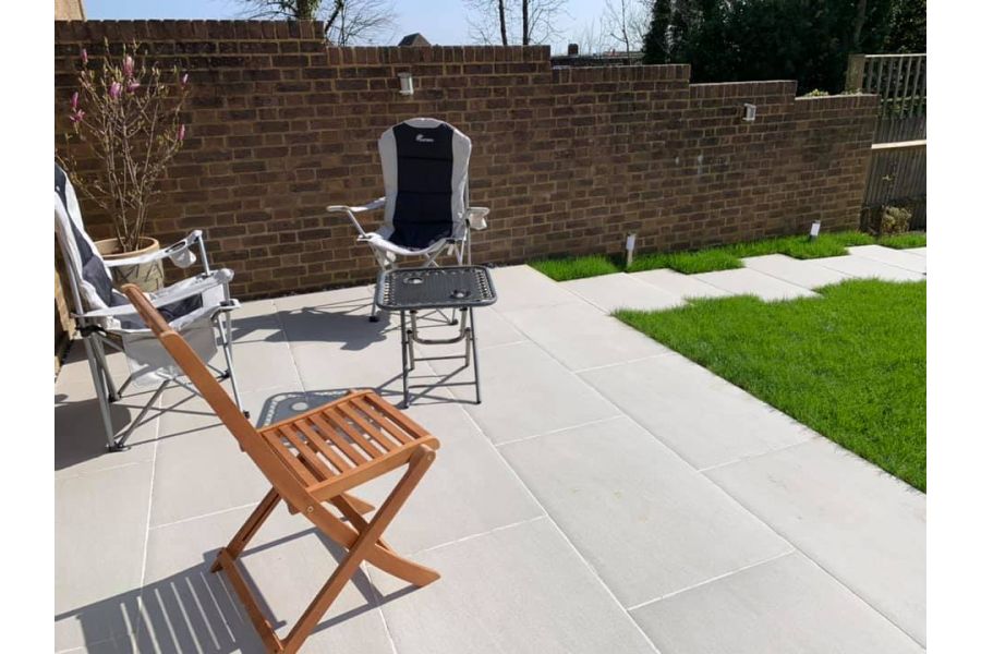 Florence Grey porcelain tiled path leads along lawn edge to paving with folding chairs and table. Design by A and G gardening.