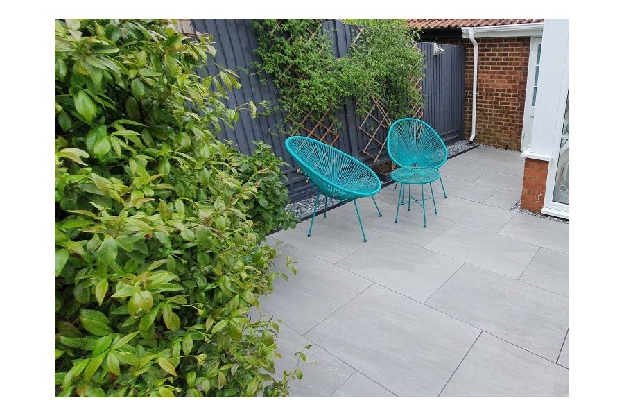 Kandla Grey Porcelain paving, with turquoise wire chairs and table against fence with trellis, designed by Absolute Landscapes.