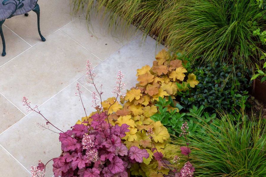 Corner of Jura beige limestone paving edged with grasses and colourful heucheras. Design by Sarah Kay. Built by Acacia gardens.