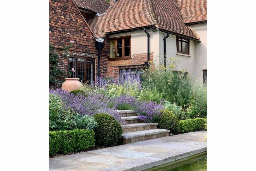 4 steps descending between dense planting at back of country house to long, narrow terrace of tumbled Black sandstone paving.