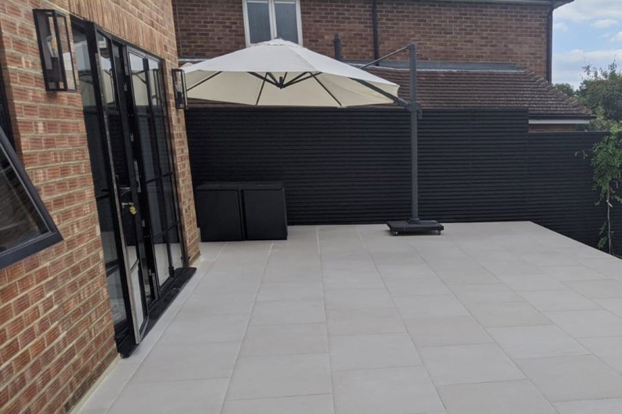 Patio doors open onto Florence White Porcelain paving patio by Adsun Landscaping, with cantilevered cream parasol next to fence.