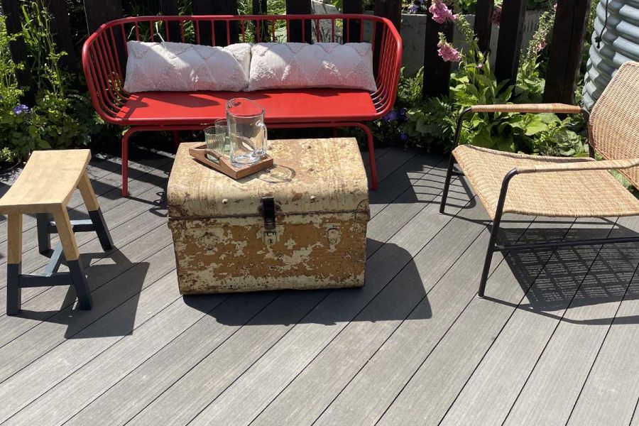 Distressed trunk coffee table with stool, red 2-seater and armchair sit on Charcoal DesignBoard composite decking laid diagonally.
