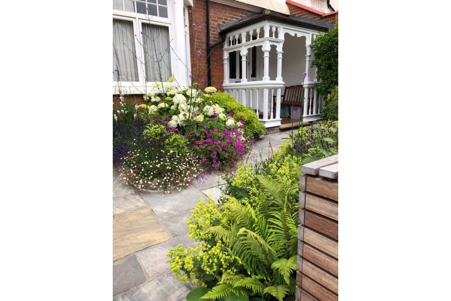 Front garden of Edwardian terraced house with Tumbled Black sandstone paving slabs leading between planted beds to wooden porch.