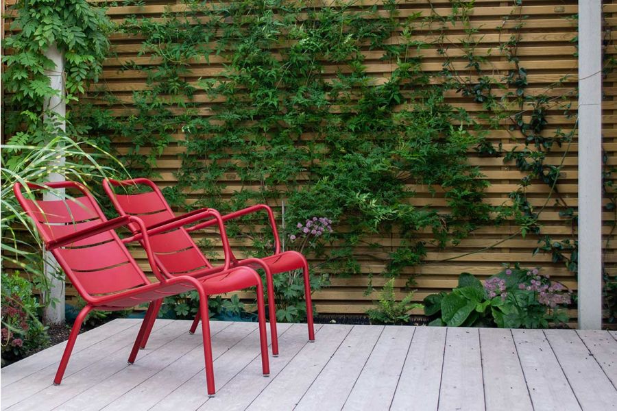 2 red metal chairs next to slatted fence with climbers, sit on Cinnamon DesignBoard composite decking. Built by Life in the Garden.