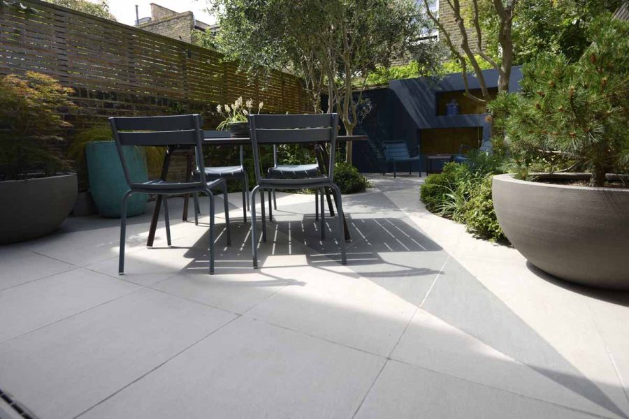 Chic courtyard garden, incorporating trendy black and urban grey porcelain tiles in angular cuts, complemented by surrounding fences and trees for privacy.