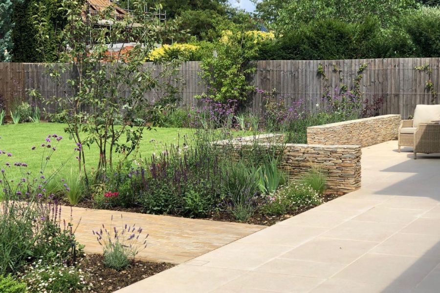 Florence page porcelain patio, partially edged with dry stone walls, accessed by clay paver path between flower beds and lawn.