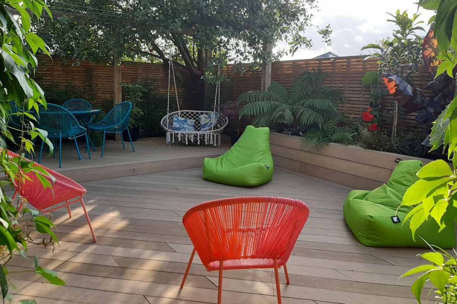 2 green beanbags and 2 orange chairs sit on Amber Classic DesignBoard WPC decking in garden with swingseat and slatted fencing.