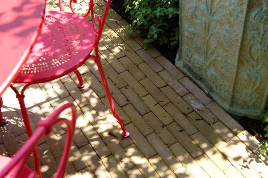 Red metal bistro chair sits on Westminster Clay Pavers, with ornate planter on adjacent border. Design by Amelia Bouquet.
