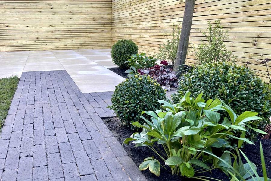 T-junction of Amersham clay pavers laid in strips separating planted bed from pale paving slabs. Design by Bark Brick and Block.