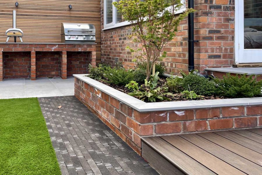 Amersham dark grey clay pavers lead from decking to porcelain paved kitchen area past brick raised bed. Built by Bark Brick Block.