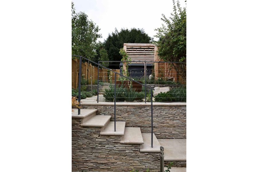 Bullnose steps adorned with cobblestone cladding leading to a verdant patio area with corten steel water feature.