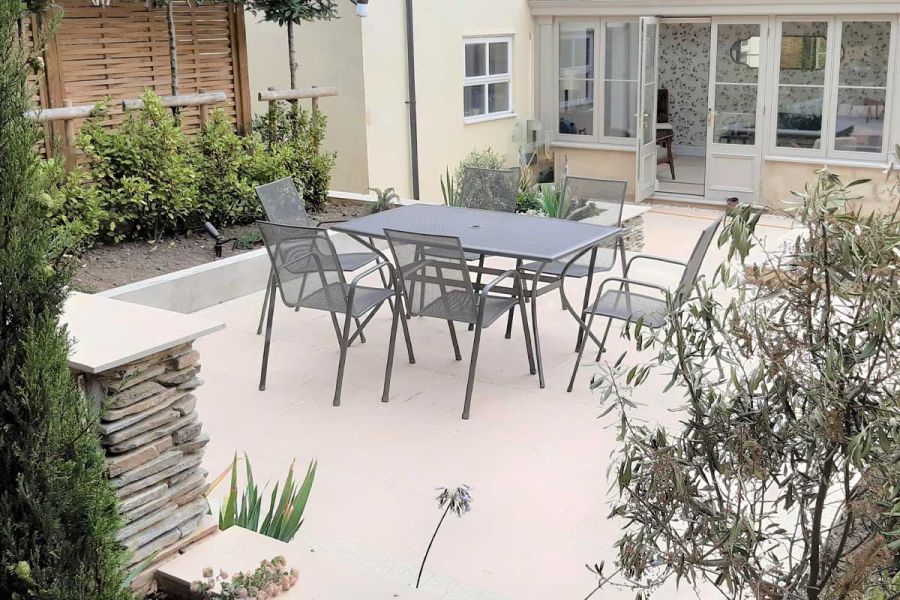 A raised patio in Florence White porcelain slabs, dressed with a metal furniture dining set, surrounded by raised planter beds.