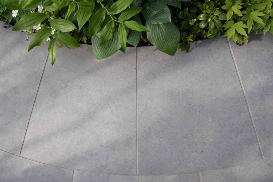Radius-cut Anthracite 800x800mm porcelain paving slabs at edge of path, with matching grout, creating curve to lushly planted bed.