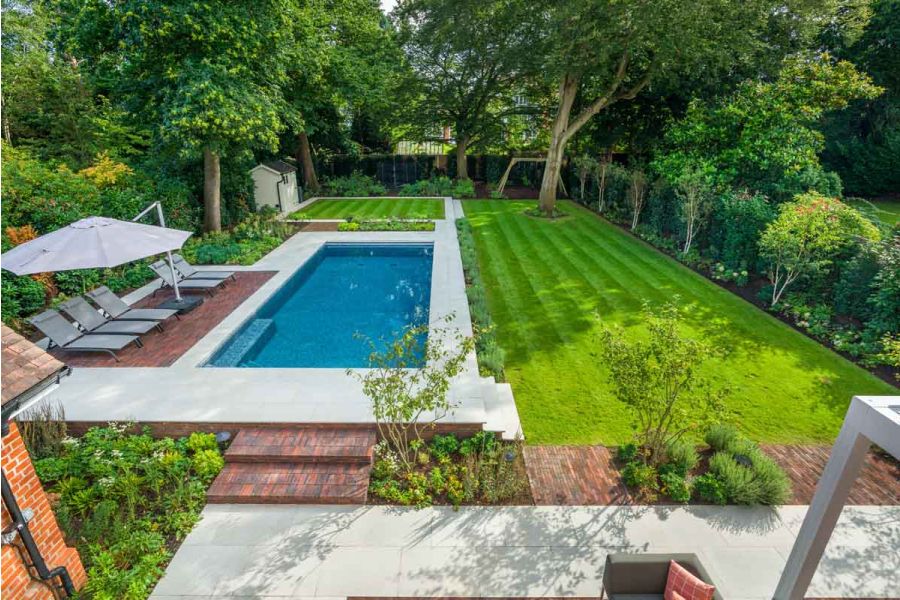 On left of long garden, grey paving surrounds swimming pool. Sun loungers sit on rectangular inset of Antique Red clay pavers.