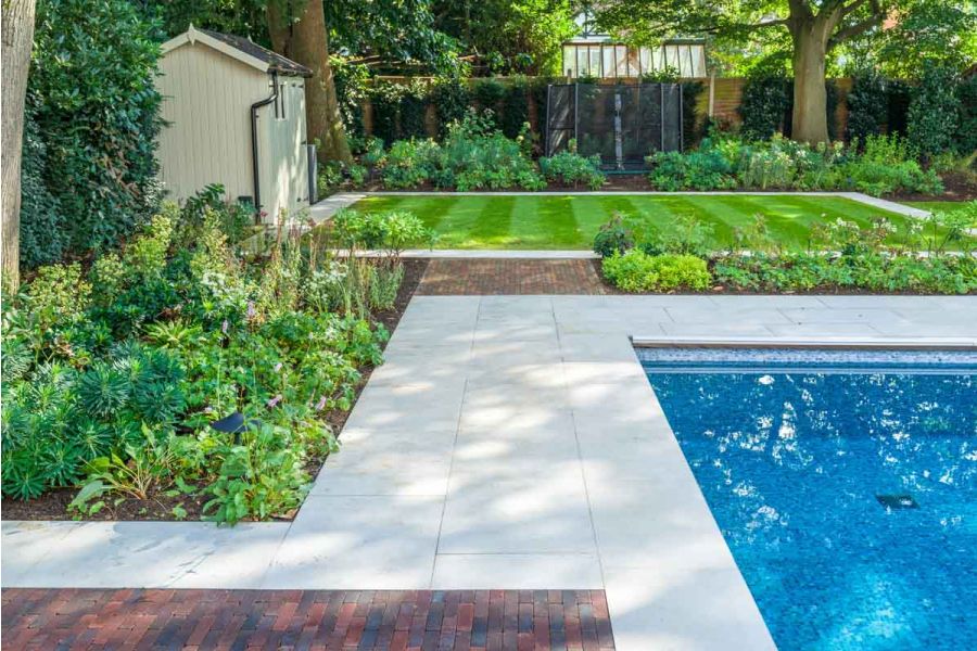 Corner of swimming pool edged with grey sandstone that is connected to matching path by wide block of Antique Red clay pavers.