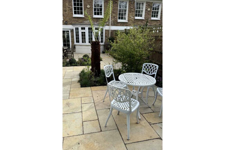 White metal table and four chairs sit on Antique Yellow Limestone Paving, withoutset planting areas, house in the background.
