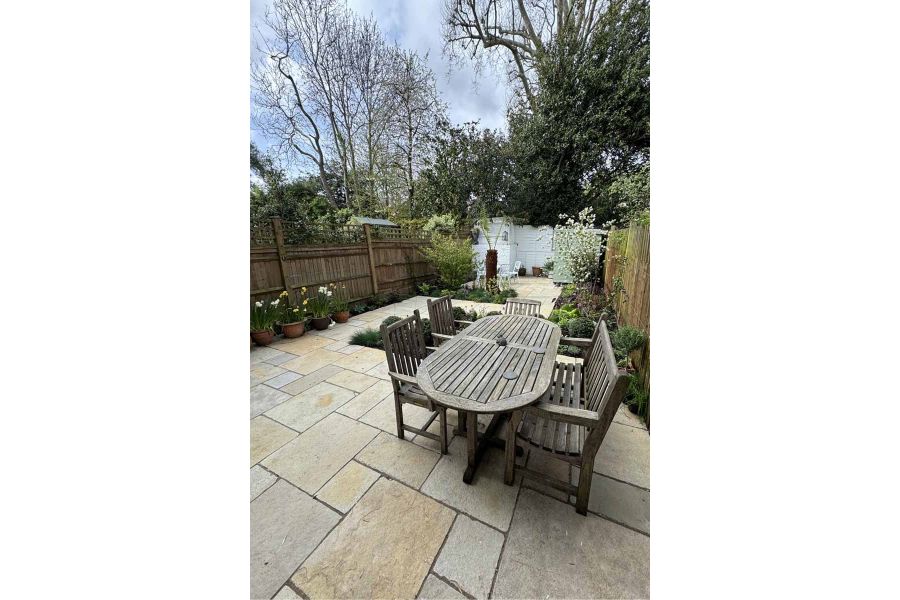 Five seat wooden table and chair set with antique yellow limestone paving in long garden with painted white brick walls.