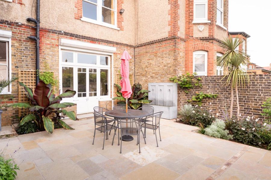 Patio by Kiwi Landscapes, in Antique Yellow Limestone paving, with metal garden furniture, at rear of Victorian terraced house.