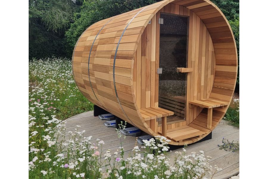 Cylindrical shepherd’s hut on round deck of grey Driftwood Millboard planks, surrounded by meadow planting.