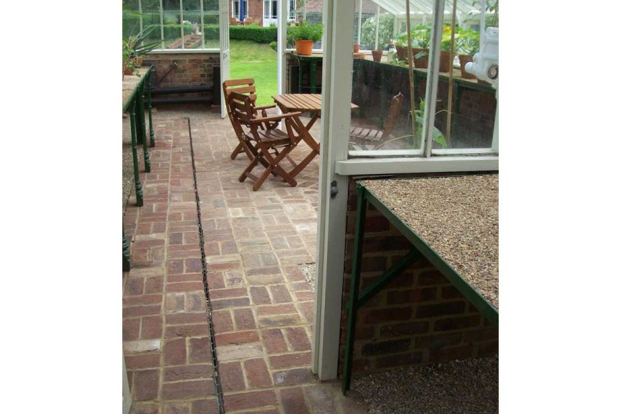 Interior of half-walled greenhouse, paved in Old English Clay Pavers laid basketweave, with slot drain. Design by Arun Landscapes.
