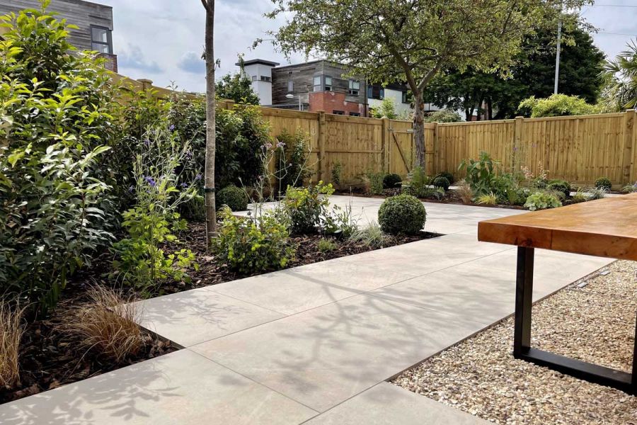 Rear city garden paved with Ash Beige Porcelain and extensive low level flower beds and closed board fencing panels.