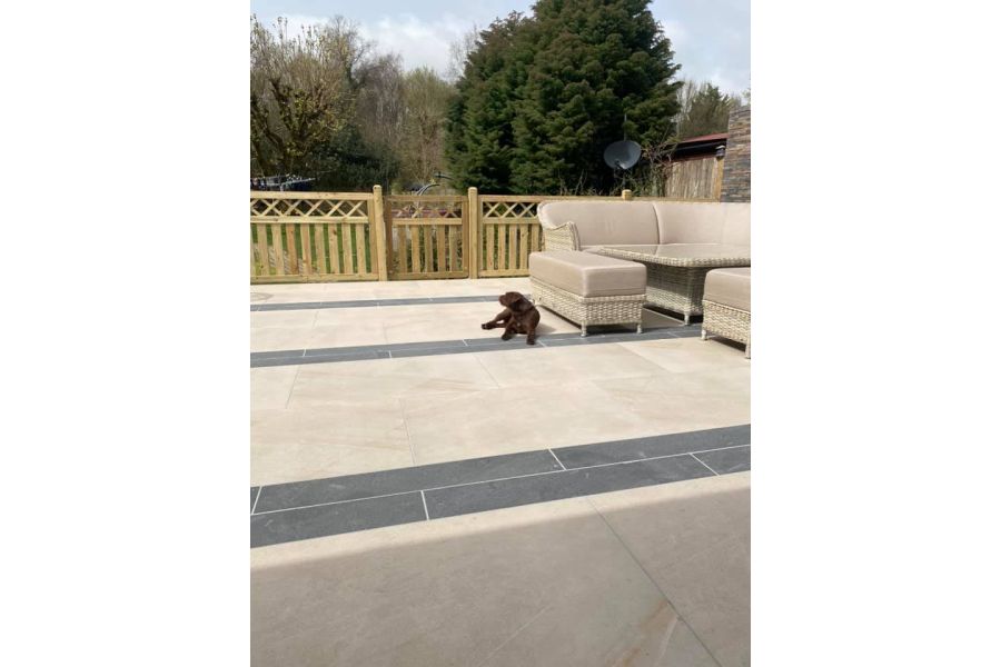 Dog sitting on top of a light coloured porcelain patio with contrasting double width strips of darker porcelain paving set at intervals.