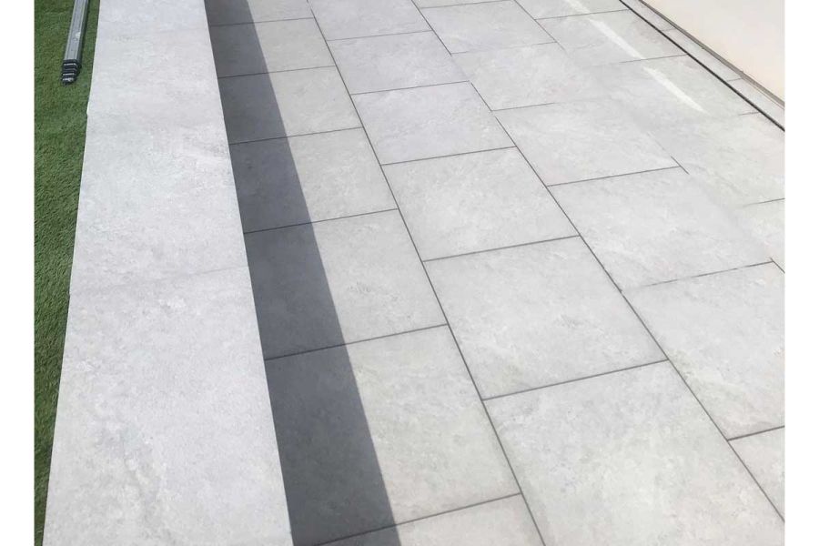 Close view of Astor Grey porcelain paving, slot drain next to white wall. Low wall in matching coping casts shadow onto patio.