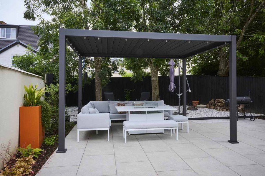 Grey pergola, with garden furniture sitting on astor grey porcelain paving with flowerbed lining the wall of the garden.