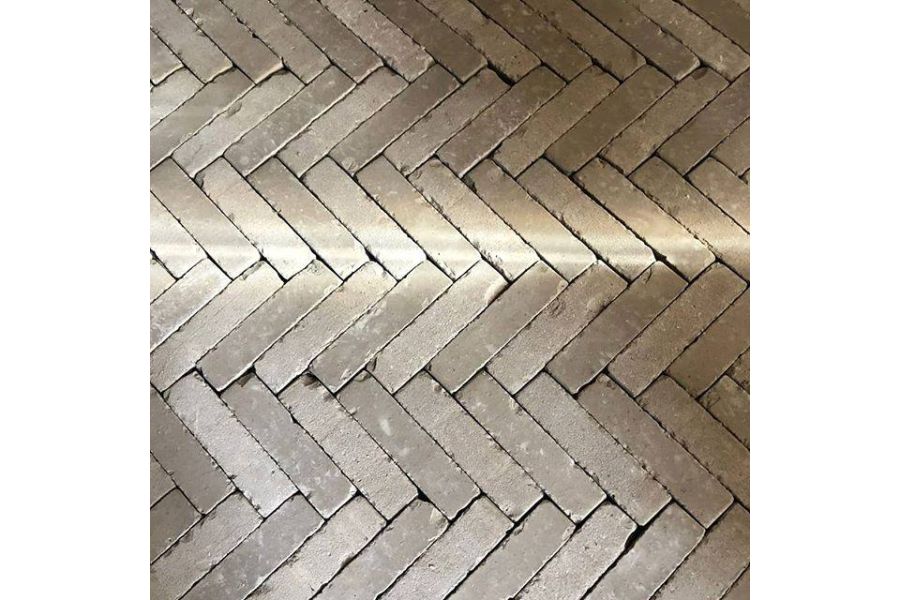 View from above of stone grey brick paving laid in herring bone pattern with shaft of light across surface. Laid by Atelier West.
