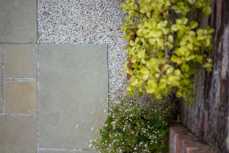 View from above of Yellow Limestone paving slabs next to pale gravel and plants against brick wall. Built by Austin Landscapes.