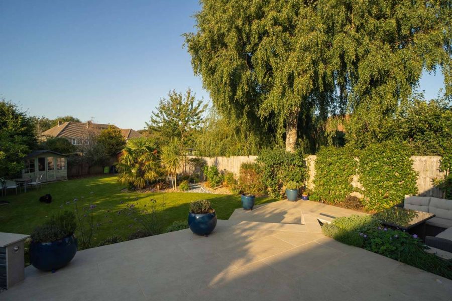 Lawned garden seen from wide terrace with patio below, paved in Golden Stone Porcelain tiles, designed by Austin Landscapes.