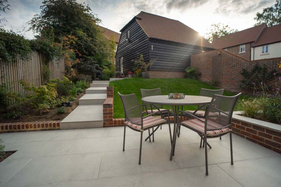 Light Grey Porcelain stepped pathway leading down from a timber clad house to a slightly sunken patio seating area.