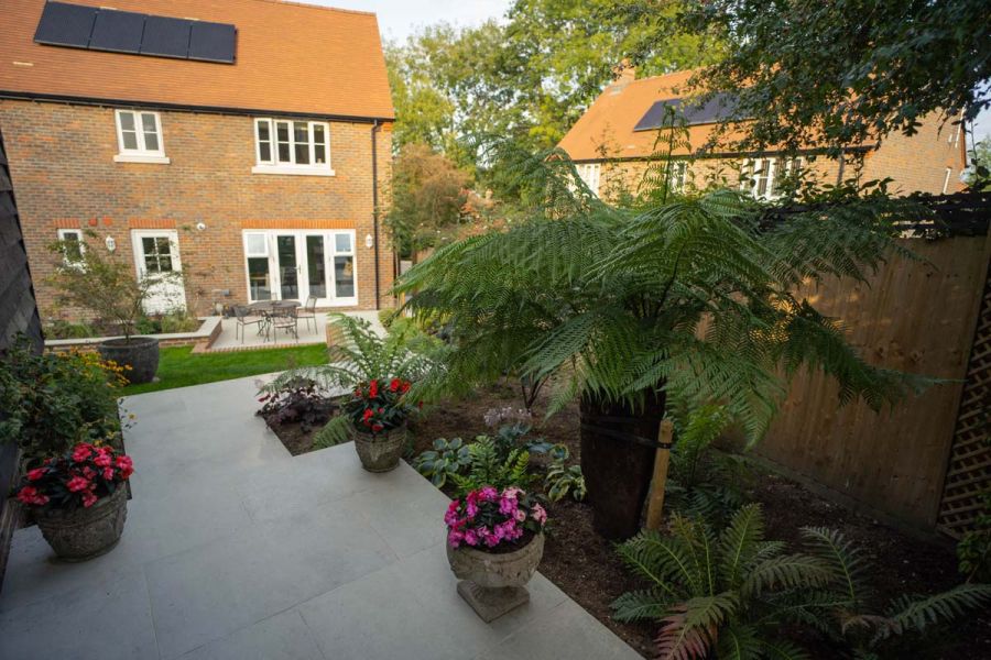 Small Porcelain patio with an adjoining large flower bed looking down towards a red bricked house.