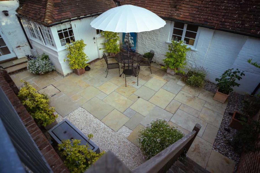 Metal dining set and parasol sit on Antique Yellow tumbled limestone paving in small courtyard of white-painted cottage.