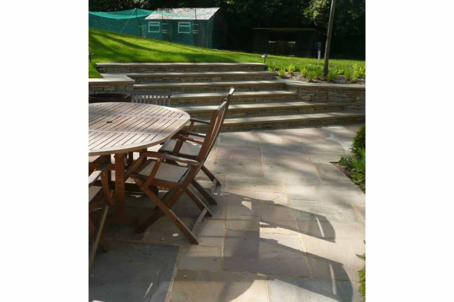 Wooden dining set sits on Autumn Brown Indian sandstone paving with 6 wide matching steps rising to large lawn with shed at rear.
