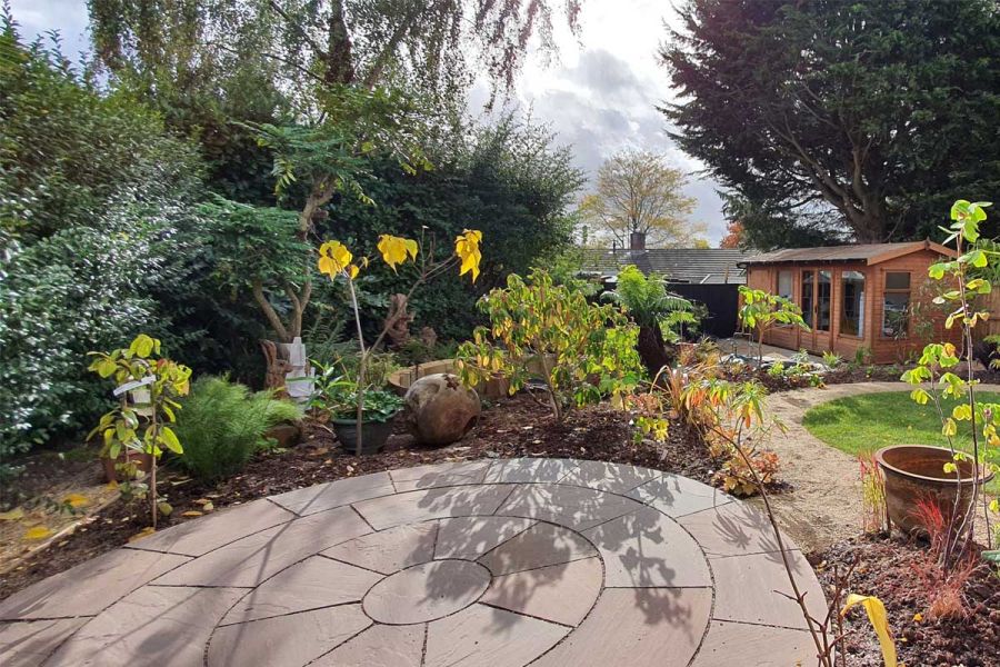 Autumn Brown Sandstone paving circle, edged with upright sleepers. Ferns and plants in arrayed in pots. By No.30 Design Studio.