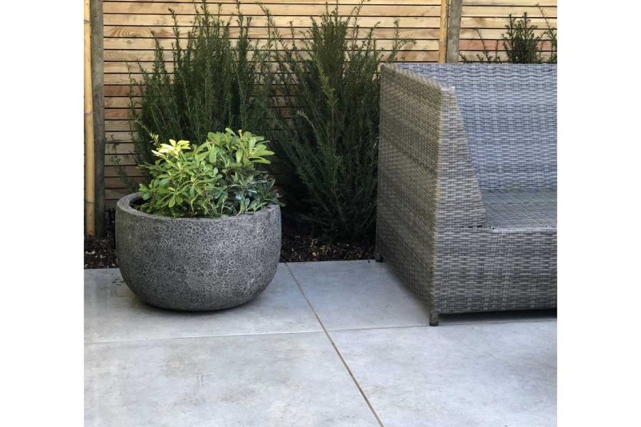 Wicker garden sofa in front of a flower bed planted with Heather sitting on top of a Polvere porcelain patio.