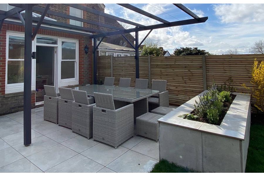 Patio doors leading out to a porcelain patio dining area set underneath a pergola with a raised planter bed and slatted fencing panels.