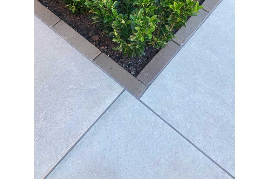 Precisely cut Florence Grey porcelain paving, bordered with contrasting coloured clay pavers that surround green plants in soil
