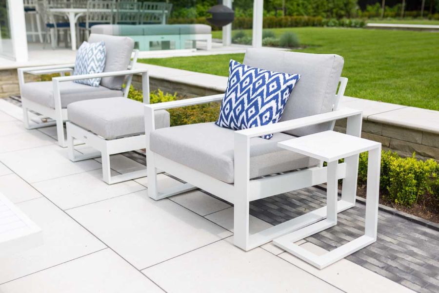 2 Contemporary white outdoor armchairs with tables either side. Grey clay pavers line a patio of Florence White Porcelain Paving.