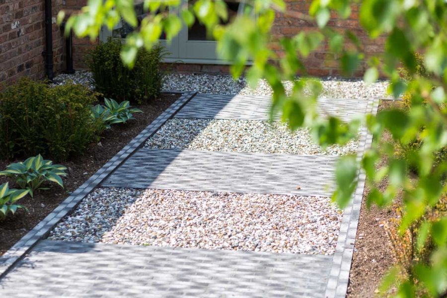 Path of wide stripes of gravel and Silver Grey Multi clay paving, edged with 2 courses of pavers, between planted beds.