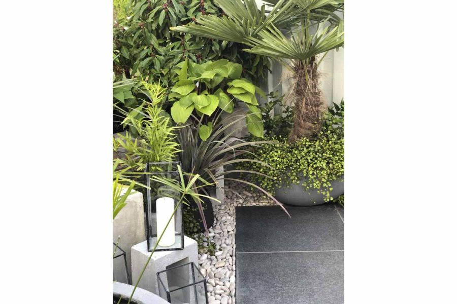 Garden corner with white pebbles contrasting with dark basalt paving, planting inspired from Brazil and candles in glass holders.